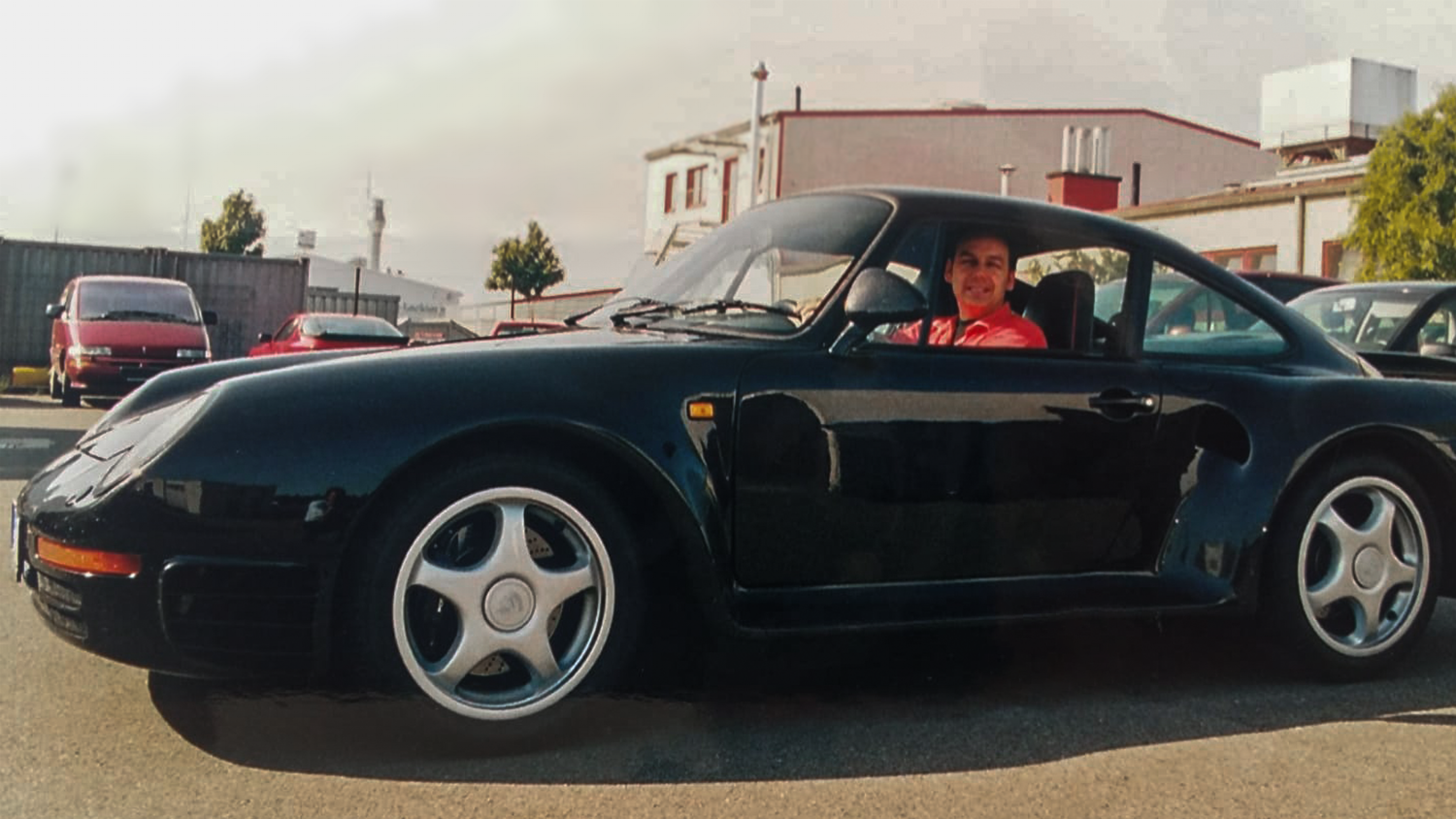 Historisches Foto: schwarzer Porsche mit Fahrer vor einer Werkshalle